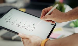 Hand holding a stylus over a digital checklist on a tablet screen.
