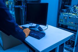 Technician typing on a keyboard at a white desk in a data center with server racks nearby
