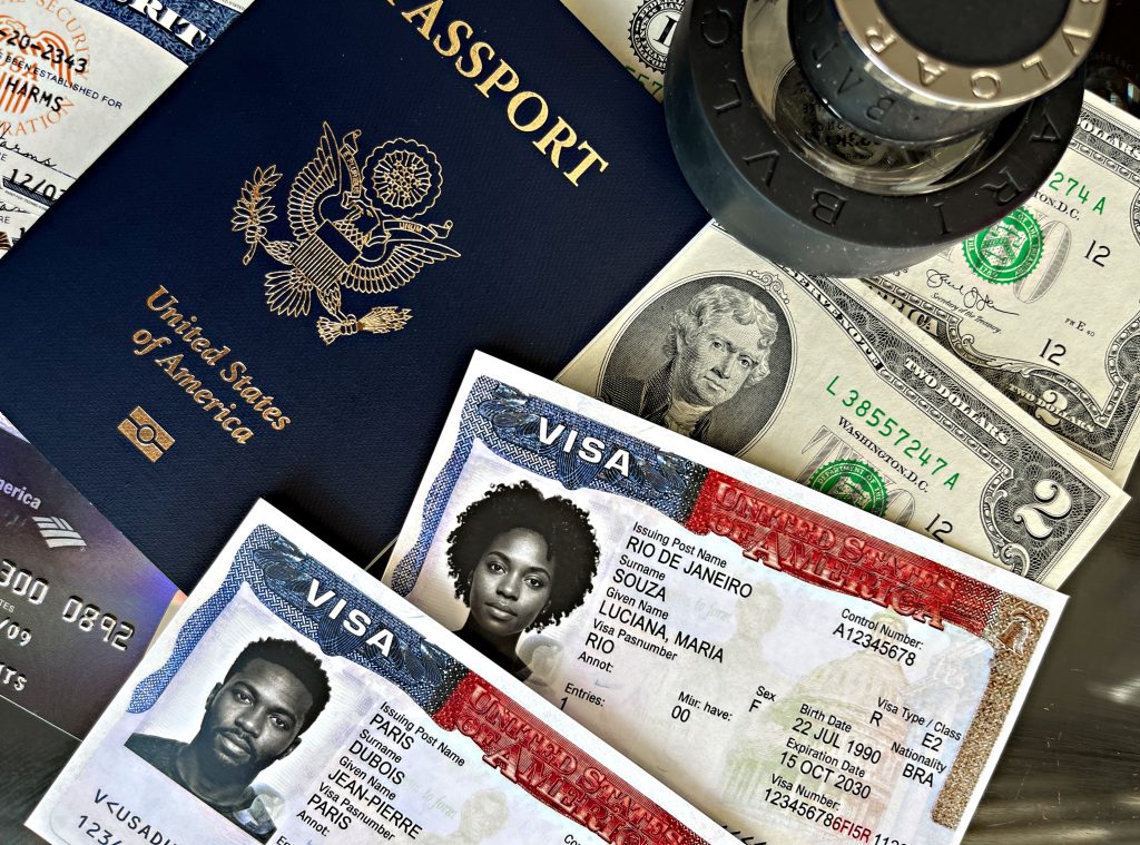 Close-up of a United States passport beside scattered U.S. dollar bills and visa cards, suggesting travel documents and money for travel.