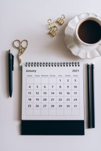 A desk calendar sitting beside a black click pen, representing scheduling and deadline tracking.