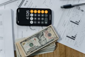 Cash money and a calculator resting on a white paper printout, representing trust accounting and reconciliation.