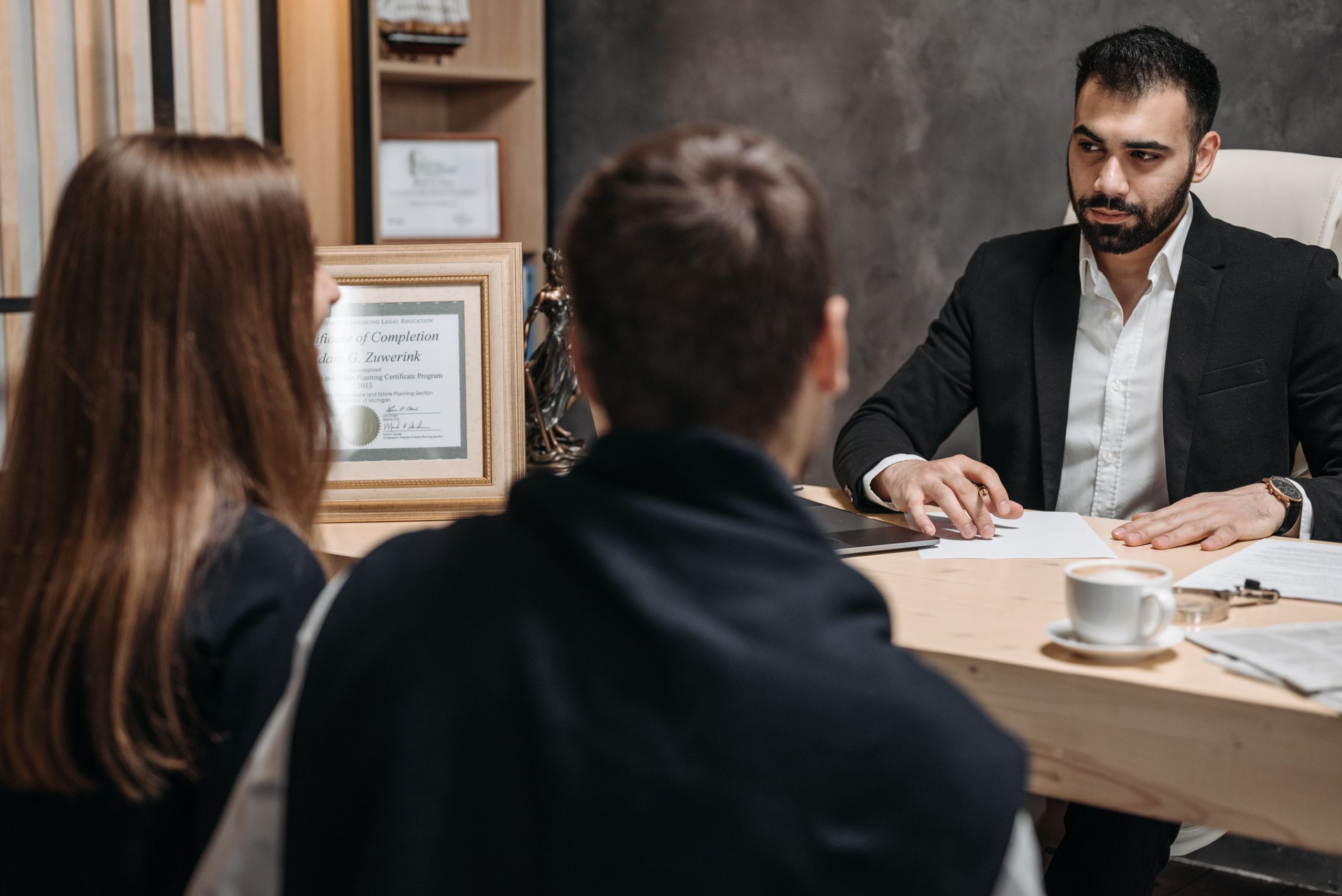 Attorney meeting with two clients in a modern law office, reviewing documents together at a desk.